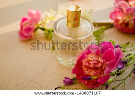 Perfume bottle with a gold cup and peony flowers on a grey background