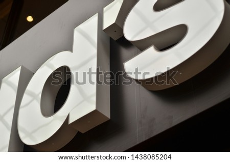 sign or logo on an exterior wall of a commercial building. The capital letters in the sign are white illumination. 