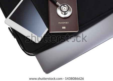 Computer notebook in black  bag ,white tablet pc, passport and medical stethoscope isolated on white background with clipping path. Online medical, travel insurance or immigration concept. Top view.