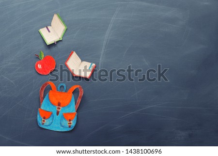 education and back to school concept. shapes cut from paper and painted of backpack, books and apple over classroom blackboard. top view, flat lay
