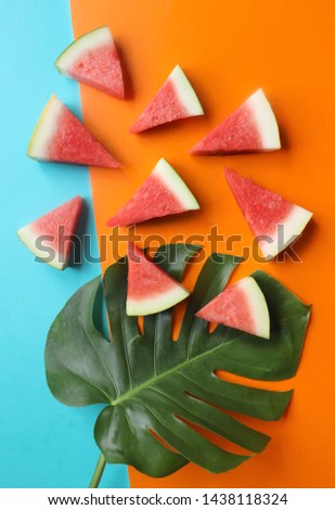 It is a photograph, from the top of a green leaf with slices of watermelon on a blue and orange background
