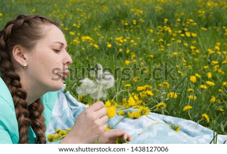 Young girl with braids blowing on white dandelions. The girl is lying on the bedspread on the grass. fun with flowers