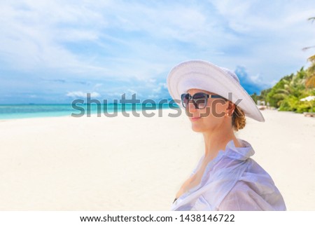 Young woman wearing straw hat enjoying vacation at beach. Portrait of beautiful woman relaxing at beach with sunglasses. Close up portrait of a smiling elegant woman with hat at a tropical beach. 