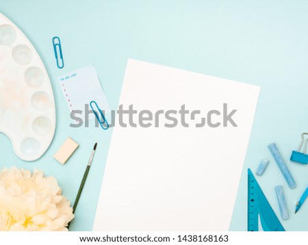 Back to school, education concept. Stationery, school tools near a white sheet of paper and painter brush besides isolated on blue color studio background with copy space. Flat lay, view from top.