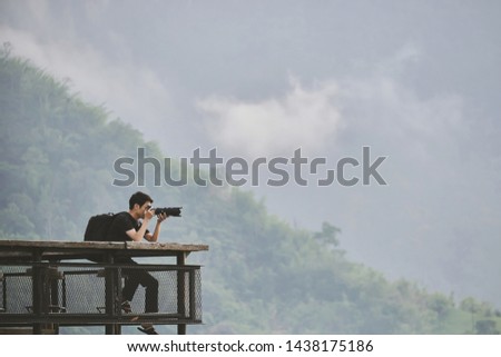 Photographer man sitting on wooden table bar and taking picture top of mountain in the morning with mostly fog. vintage tone