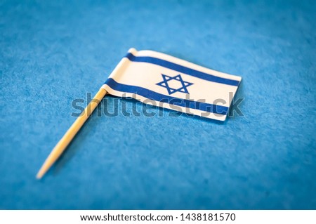A small flag of Israel on a wooden toothpick on a blue paper background, closeup image. Beautiful image of Israeli flag.