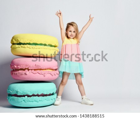 Cute little girl in bright clothes have fun at the birthday party fun room decoration candy macarons.