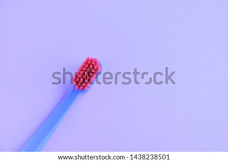 Blue plastic toothbrush with bright pink bristles with selective focus on blurred purple background with empty space for text. Toothbrush for daily cleaning of teeth and caries protection 