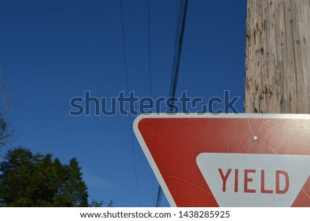 Yield sign with a blue sky in the background, obscured by a tree and a telephone pole with wires symmetrically stretched across the picture.