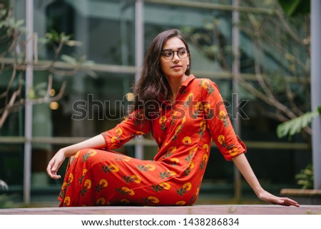 Portrait of a young, attractive Indian Asian woman in a traditional Indian orange dress smiling as she sits on a step in the city during the day. 