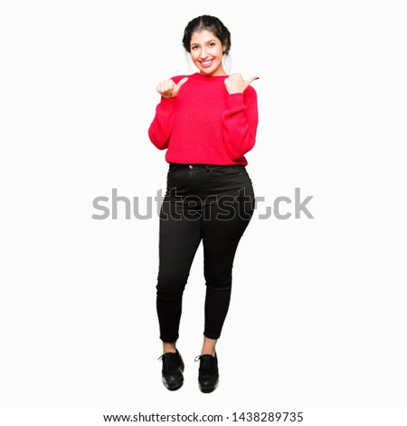 Young beautiful woman wearing red sweater and bun Pointing to the back behind with hand and thumbs up, smiling confident