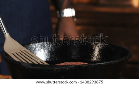 Close-up of of chef in blue apron standing near the pan grill and frying cutlet for hamburgers. Stock footage. Preparation of delicious home-made burgers