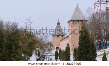 View of two old red brick towers with wooden roof and wall near the trees in in winter against grey sky. Stock footage. Beautiful Russian historical architecture