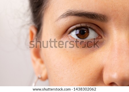 A closeup view on the eye of a beautiful young woman. A slight dark circle can be seen beneath the eye. Details of girl with brown iris. Copy space on the left.