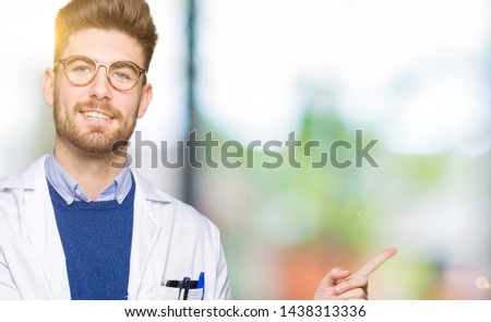 Young handsome scientist man wearing glasses with a big smile on face, pointing with hand and finger to the side looking at the camera.