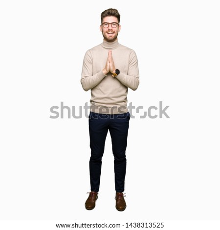 Young handsome business man wearing glasses praying with hands together asking for forgiveness smiling confident.