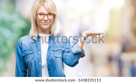 Young beautiful blonde woman wearing glasses over isolated background smiling cheerful presenting and pointing with palm of hand looking at the camera.