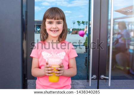 The happy lovely girl with orange juice at an entrance to cafe.