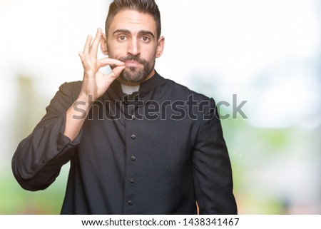 Young Christian priest over isolated background mouth and lips shut as zip with fingers. Secret and silent, taboo talking