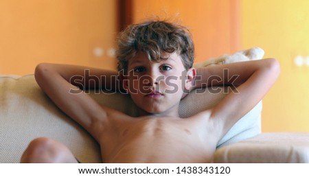 Little boy shirtless relaxing at living room sofa watching movie.