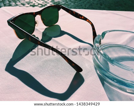 Close up photo of vintage leopard Wayfarer sunglasses and ashtray on table of street cafe summer terrace against paving stones.