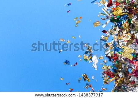Festive party or carnival border of colored, shiny serpentines and confetti on light blue background with copy space. Colored confetti flying on blue background