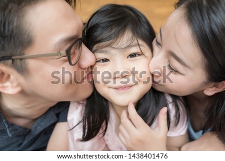 Asian Parents kissing their little daughter on both cheeks. family portrait.