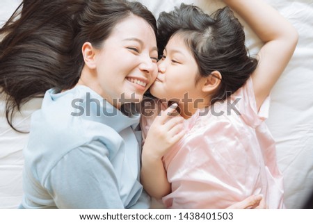 Daughter kisses her mother's cheek. and hugging in the bedroom .Happy Asian family