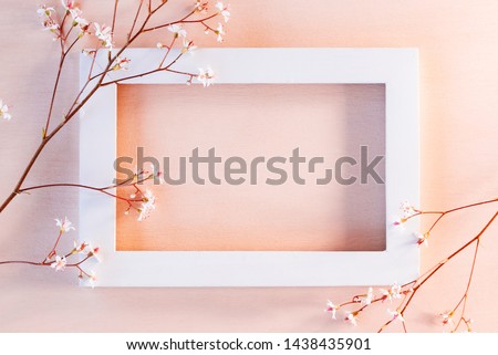 White wooden frame on a coral textured background with small flowers - a template for a greeting card or invitation