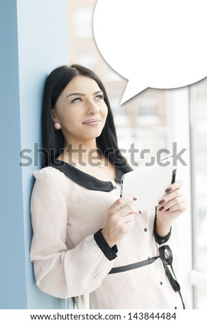 Portrait of a happy smiling young business woman using tablet PC while standing relaxed near window at her office