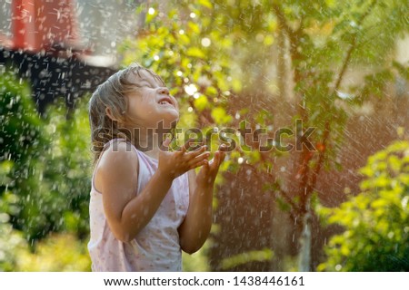 Happy child girl playing under the rain. Family have fun time outdoors under summer shower. Kid without umbrella playing with rain. Summer holiday concept.