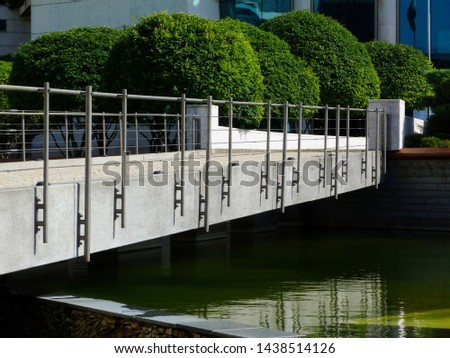 lush green sphere shaped small trees in public park with concrete and steel foot bridge of modern design and bright green water underneath. reflections on water. beautiful landscape design concept.