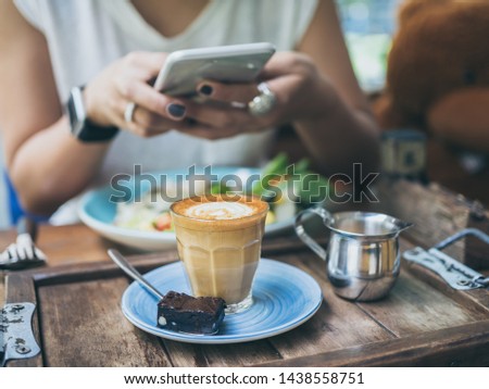 Woman's hands taking photo of coffee cup, Piccolo Latte, brownies with breakfast on wooden table by smartphone.