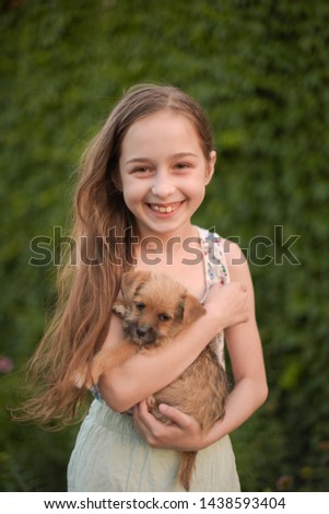 A little blond girl with her pet dog outdooors in park. The girl loves a little puppy. A dog in the arms of a child. Summer rest.