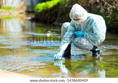 scientist researcher in protective suit takes water for analysis from polluted river Royalty-Free Stock Photo #1438600409