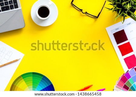 Designer office desk with tools, pallet, coffee, laptop and glasses on yellow background top view mock up