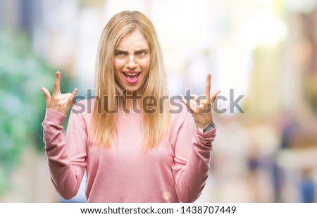 Young beautiful blonde woman wearing pink winter sweater over isolated background shouting with crazy expression doing rock symbol with hands up. Music star. Heavy concept.