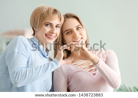 Portrait of happy mother and daughter making heart with their hands at home