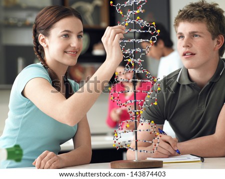 Happy teenage students examining DNA model and taking notes in science class Royalty-Free Stock Photo #143874403