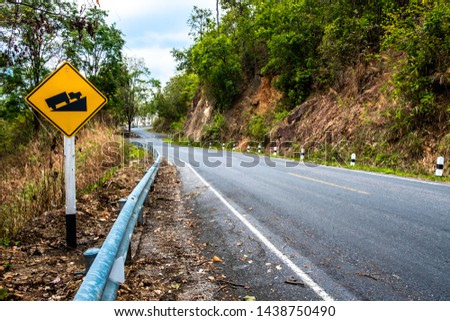 Road sign with yellow background and black illustration warning truck that uphill steep slope ahead on a curvy road.