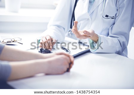 Doctor and female patient sitting at the desk and talking in clinic near window. Medicine and health care concept. Green is main color Royalty-Free Stock Photo #1438754354