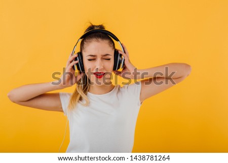 teen listening to music in headphones, in white shirt, closed eyes, isolated on yellow background, copy space