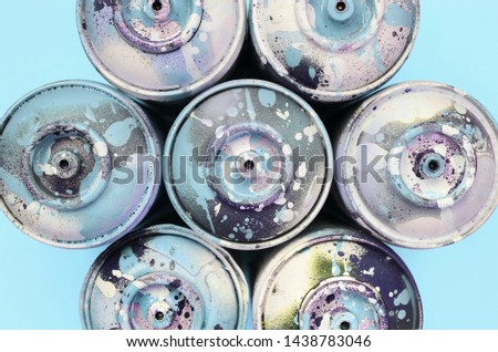 A few used spray cans with blue paint drips lie on texture background of fashion pastel blue color paper