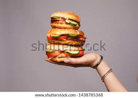 Female hand holding pyramid from three appetizing burger isolated at gray studio background closeup