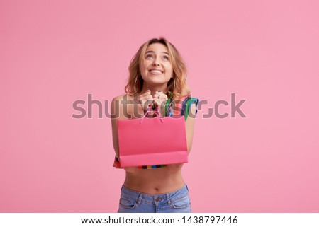 Portrait of an excited beautiful smiling girl wearing colorful clothes holding shopping bag isolated over pink background. Place to sign or text on the package