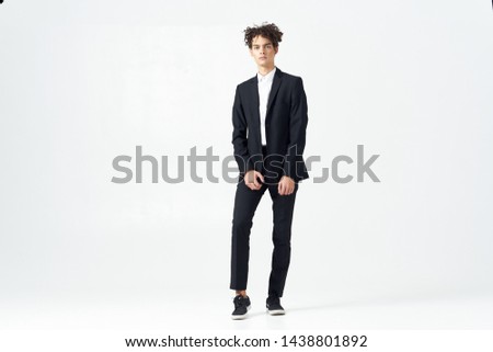 Cute guy with curly hair and in a suit standing on a light background in full growth                         