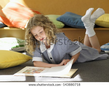 Full length of elementary schoolgirl reading book on floor in classroom