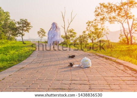Beautiful bride wearing a white wedding dress running away alone in nature outdoor with leaving a bouquet of flowers and shoes on the street. Runaway bride before the wedding ceremony concept. Royalty-Free Stock Photo #1438836530