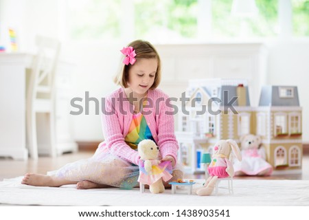 Little girl playing with doll house in white sunny bedroom. Kid with toys. Role game for young children. Child with teddy bear toy. Kids play tea party with stuffed animals and dolls. Nursery interior