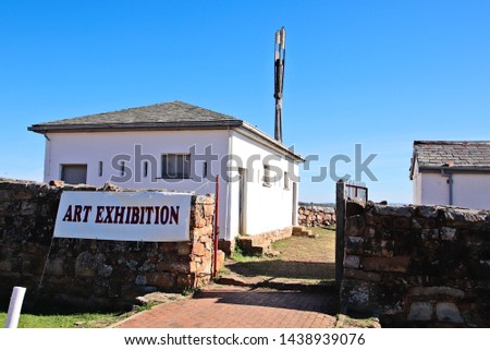 An art exhibition banner hanging on a stone wall in Makhanda, South Africa.  